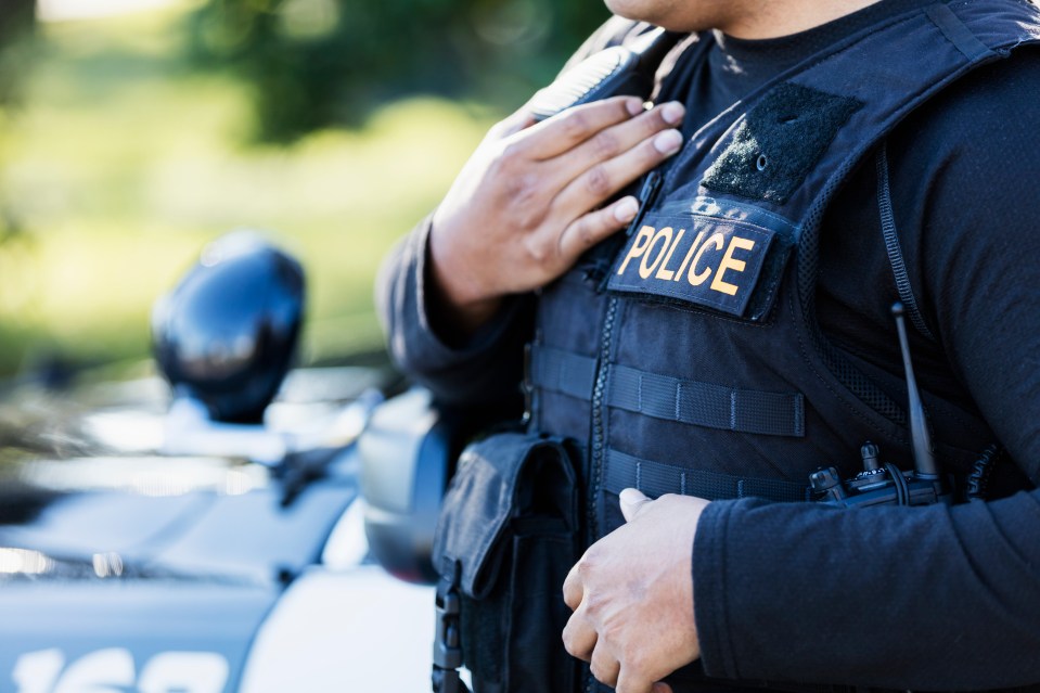 Close-up of a young Hispanic police officer's torso, hand on chest, wearing a bulletproof vest.