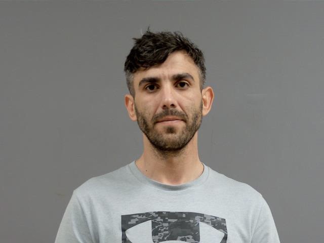 Mugshot of a man with short brown hair wearing a light gray t-shirt.