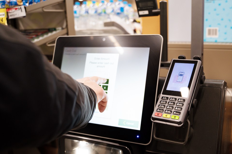 Person using a self-checkout machine in a supermarket.