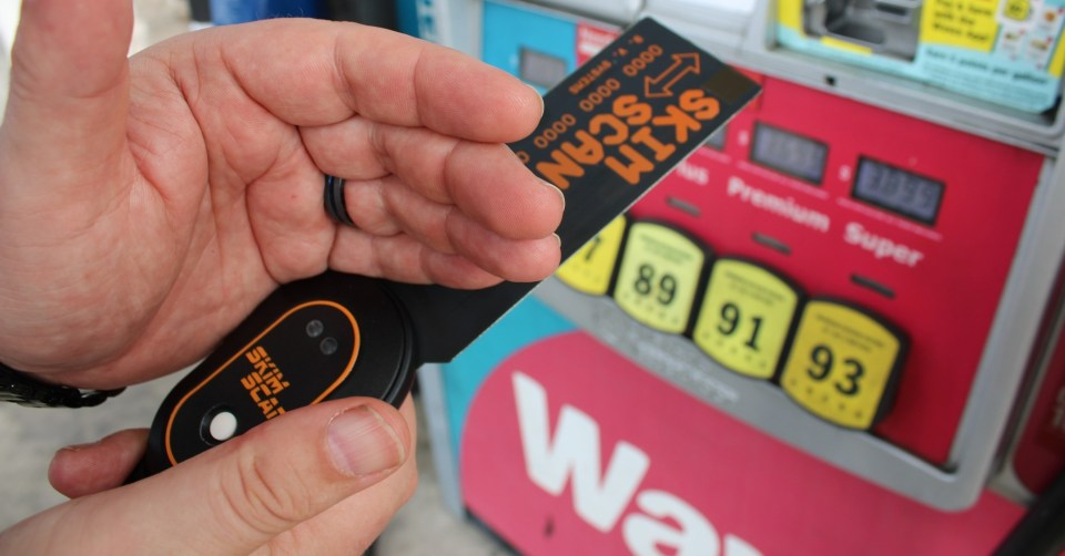 Person holding a skim reader device and gas station credit card reader at a gas pump.