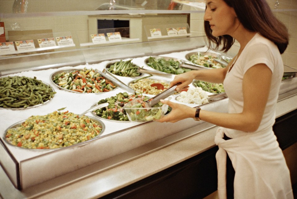 Woman preparing a salad at a self-service bar.