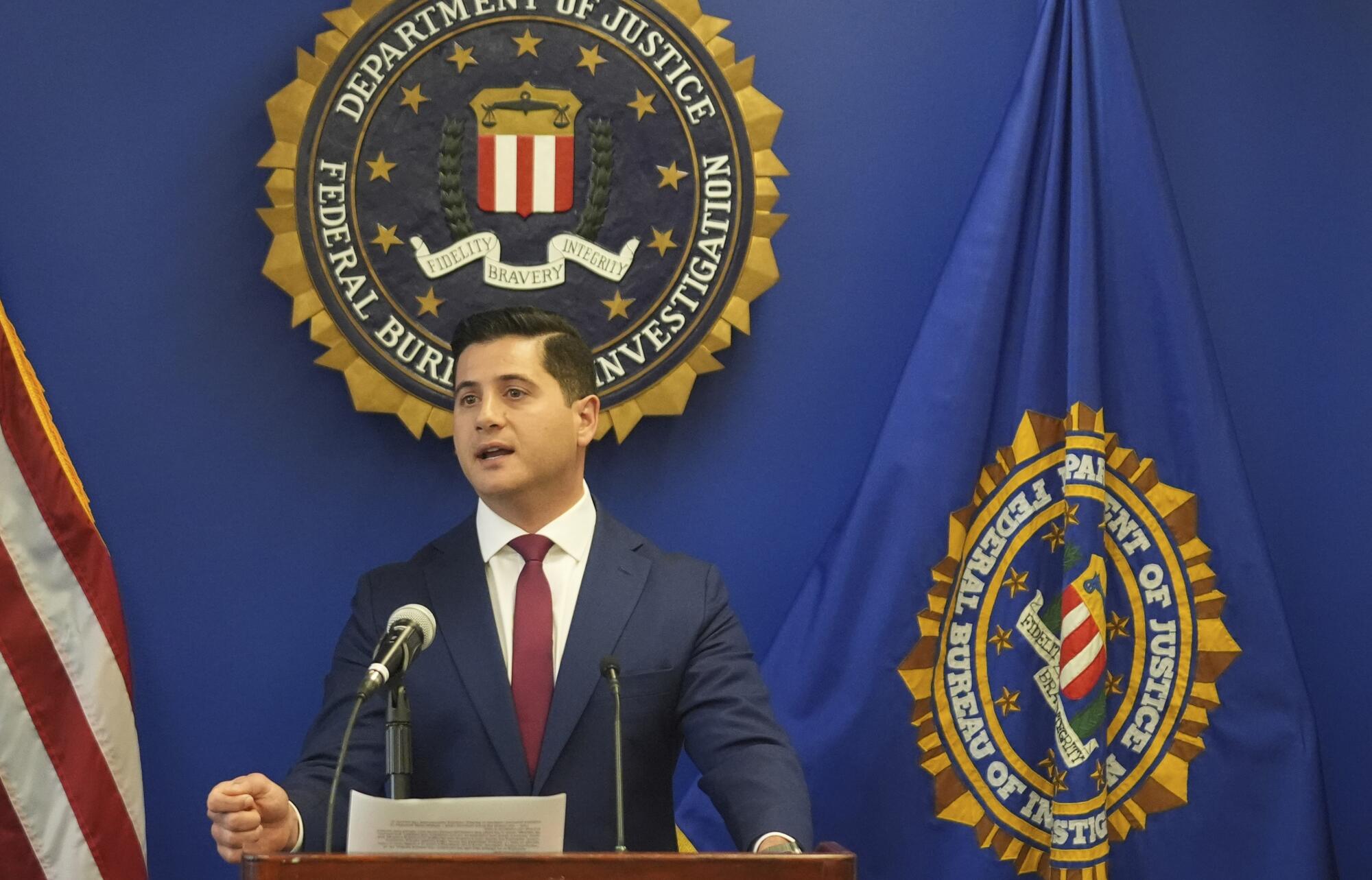 A man in a suit and tie speaks at a podium in front of the seal of the Department of Justice.
