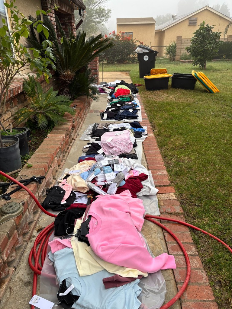 Large piles of clothing and accessories with tags still attached, possibly stolen, laid out on a brick walkway.